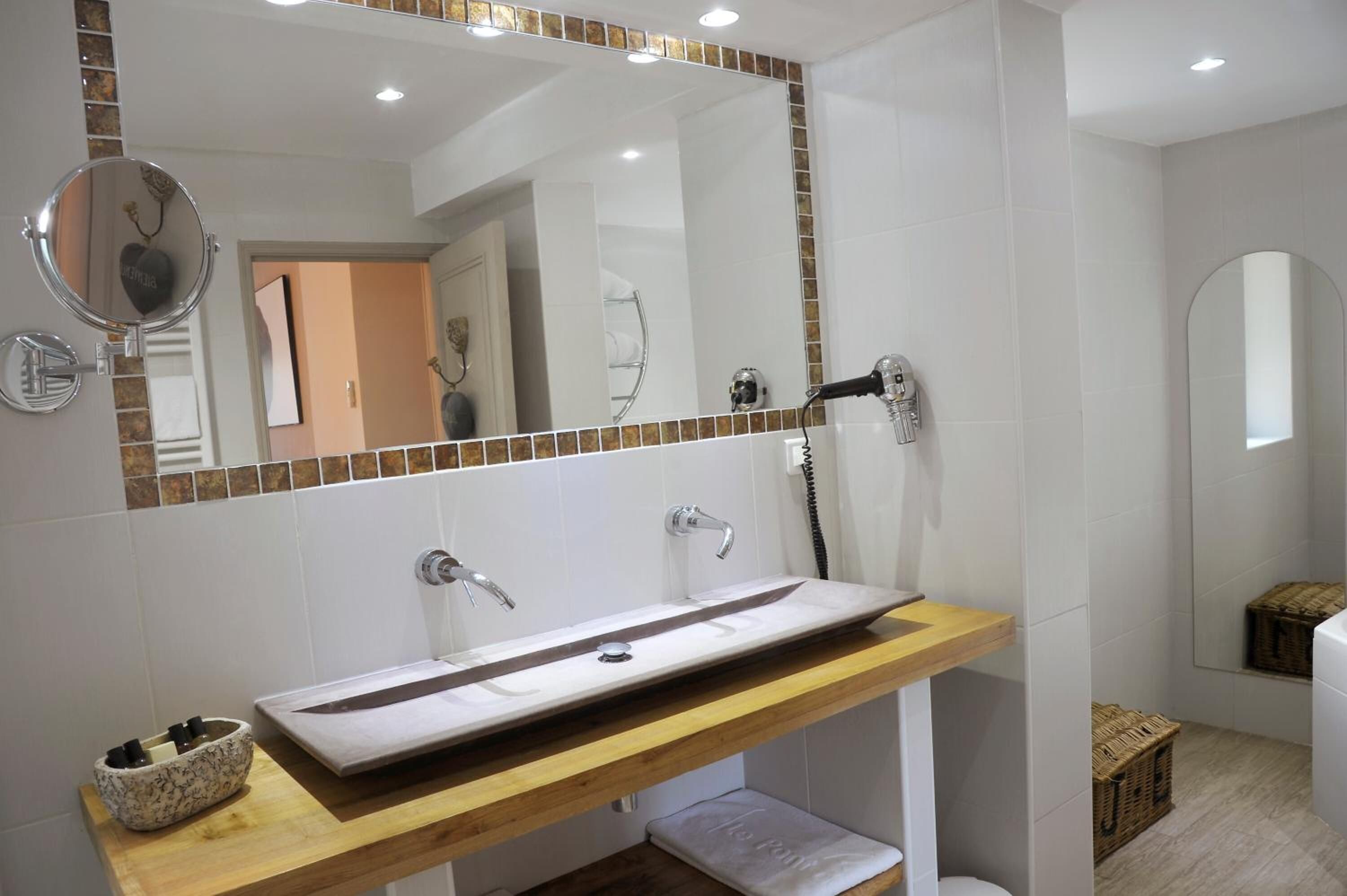 A modern bathroom with a large mirror, a vessel sink, and a hairdryer mounted on the wall.