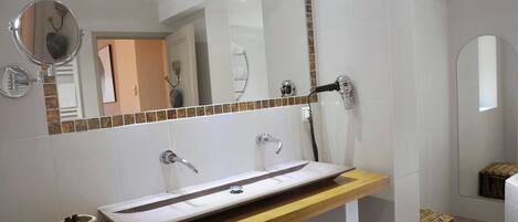A modern bathroom with a large mirror, a vessel sink, and a hairdryer mounted on the wall.