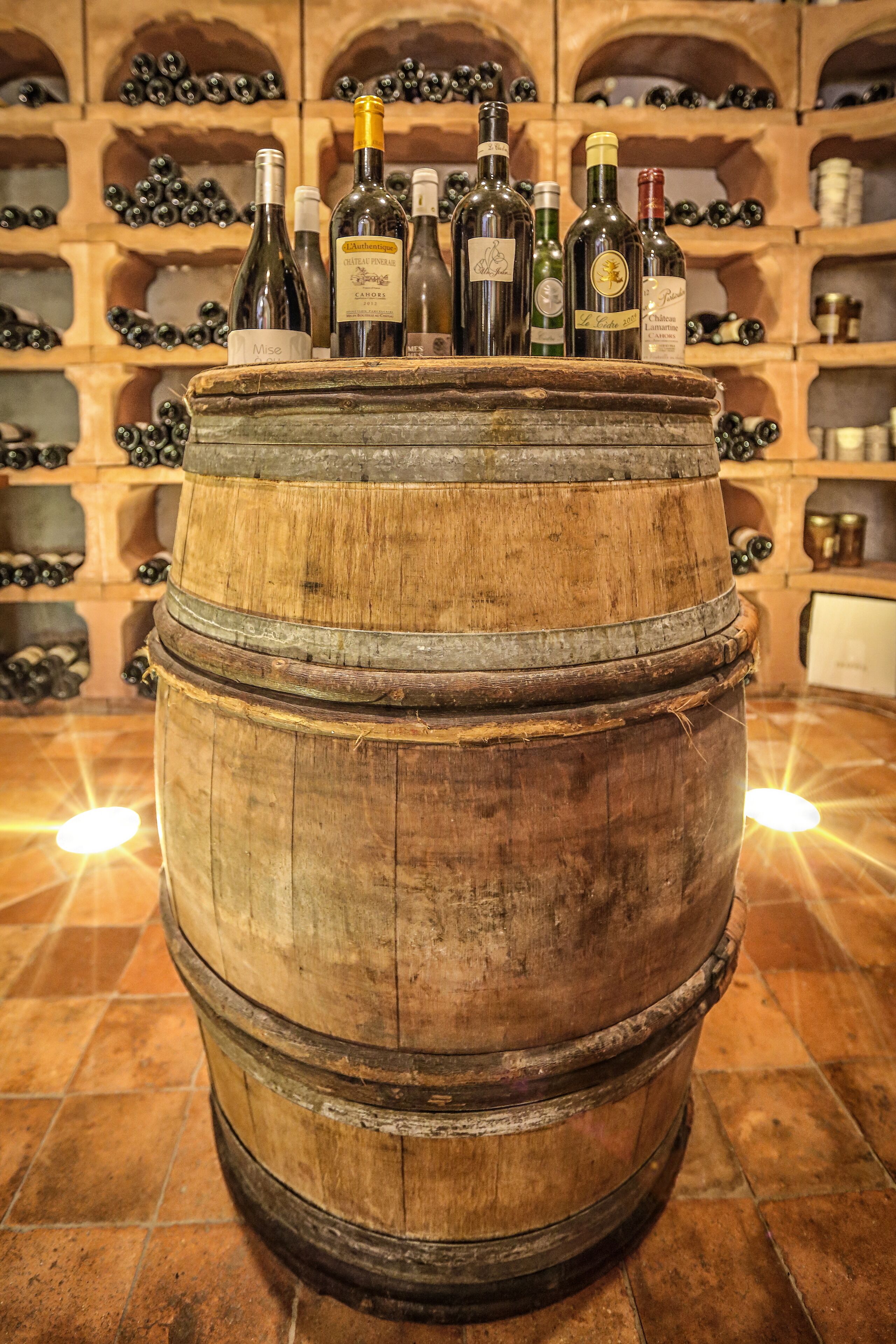 Un tonneau en bois surmonté de bouteilles de vin, le tout placé devant une étagère remplie de divers objets.