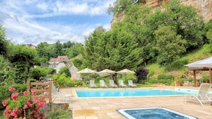 A swimming pool with lounge chairs and umbrellas, surrounded by greenery and a hillside.