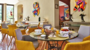 A dining area with yellow chairs, a glass table, and colorful artwork on the walls.