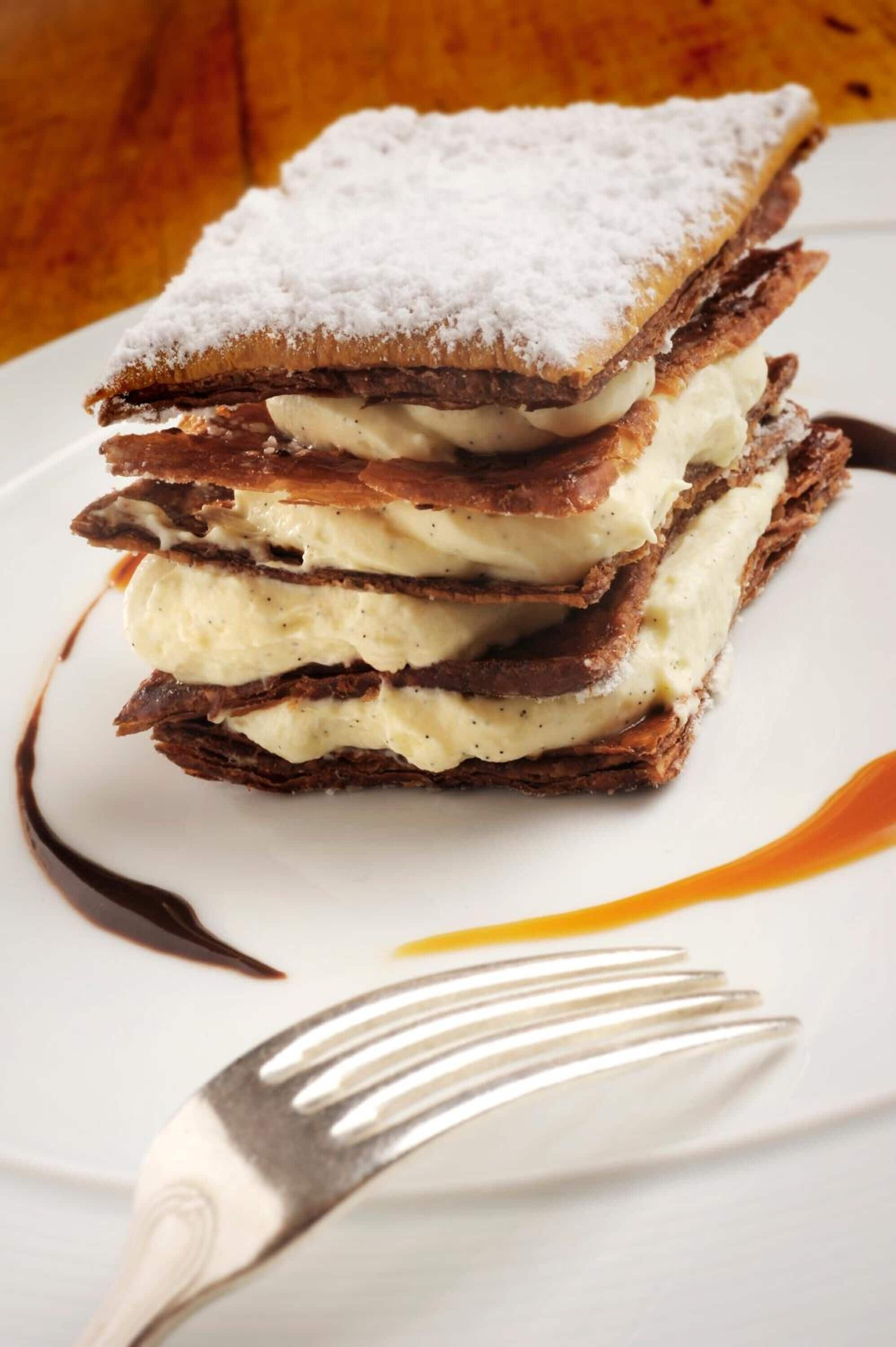 A stack of layered dessert with powdered sugar on top, served on a white plate with a fork.