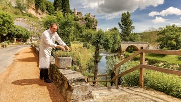 Una persona con un camice bianco in piedi vicino a un muro di pietra con vista su un fiume e un ponte.