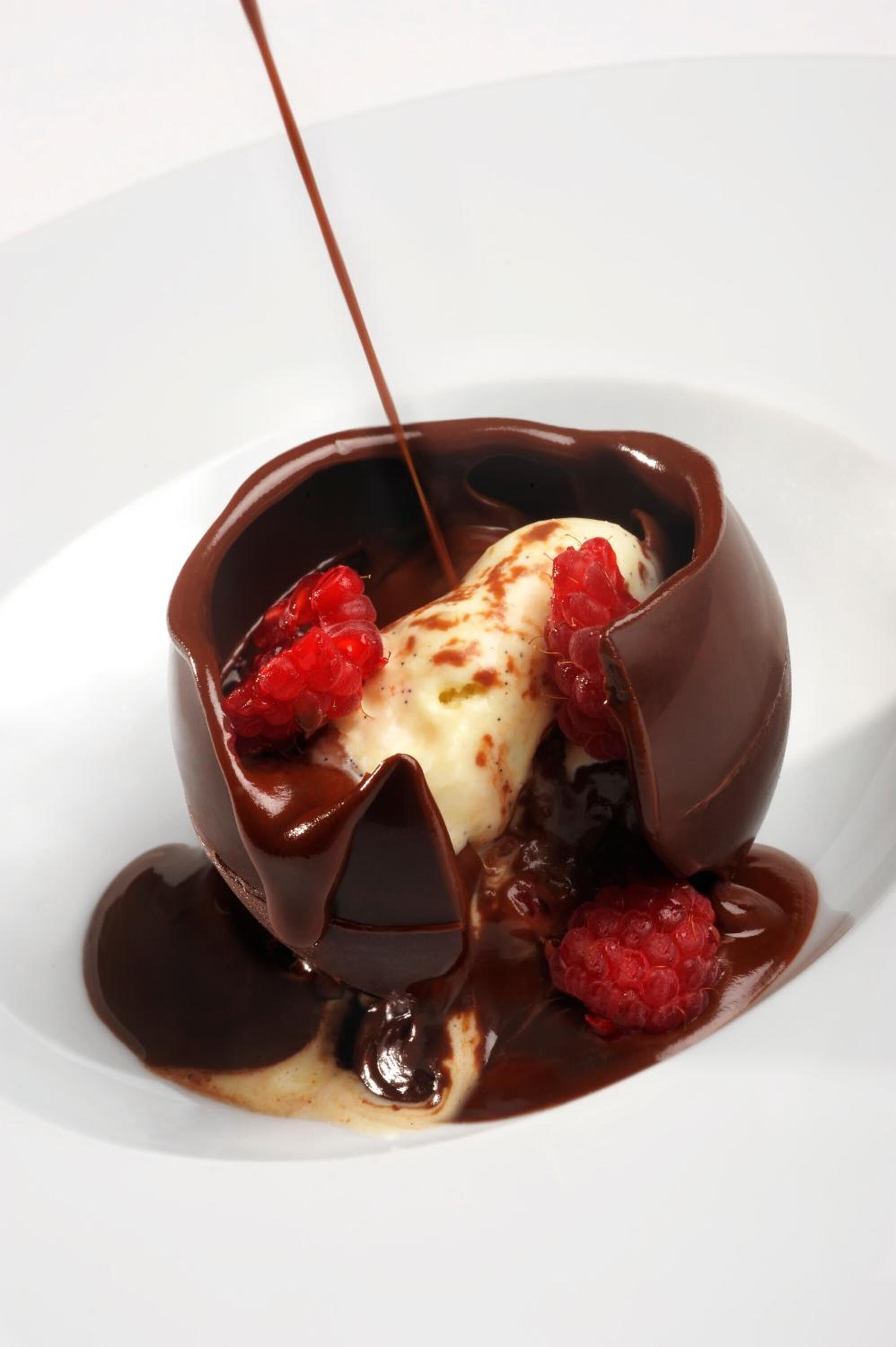 A dessert with chocolate sauce and raspberries on a white plate.