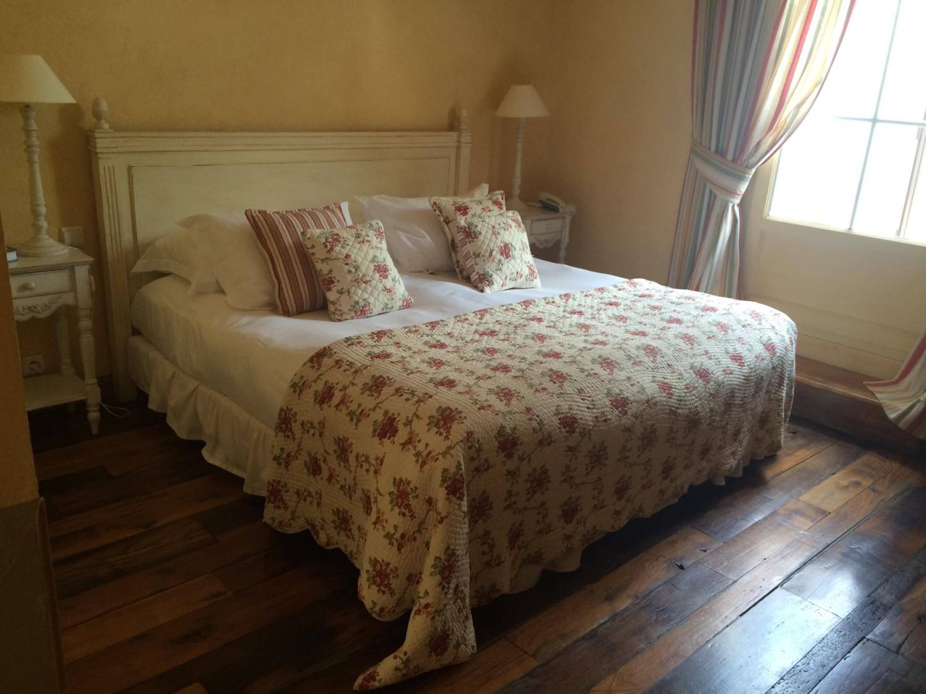 Un lit bien fait, avec une literie à motifs floraux et des oreillers, un plancher en bois et une table de chevet avec une lampe.