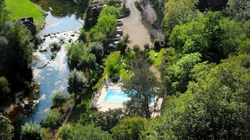 Un paysage verdoyant et luxuriant, avec une rivière, une piscine et une falaise surplombant un village.