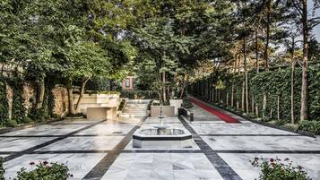 Un patio con fuente, suelo de mármol y abundante vegetación.