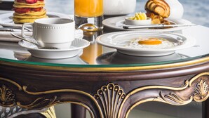 A breakfast table with a croissant, a glass of orange juice, a teapot, a cup, and a plate with a sunny-side-up egg, set against a view of a bridge and water. - Bosphorus Palace Hotel - Special Class (Istanbul)
