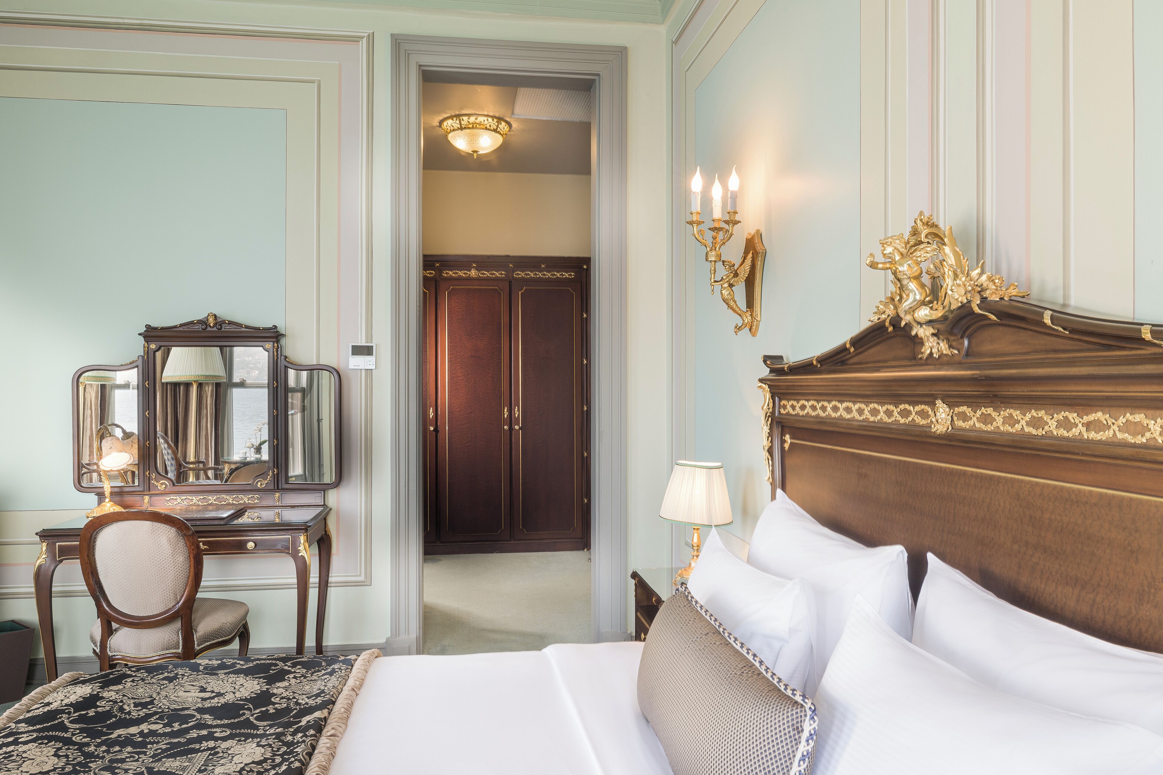 A hotel room with a large bed, a wooden dresser with a mirror, a desk, and a chair.