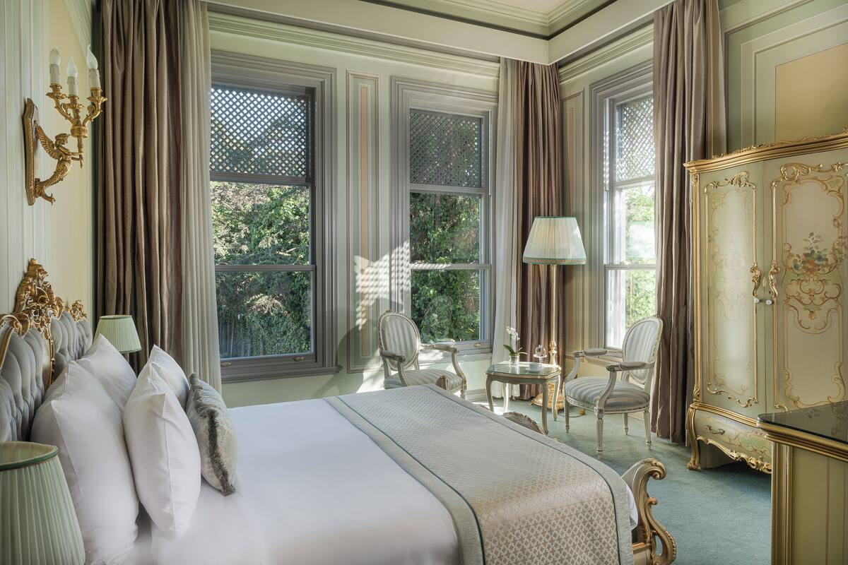 A spacious bedroom with a large bed, two chairs, a small table, and a decorative cabinet.
