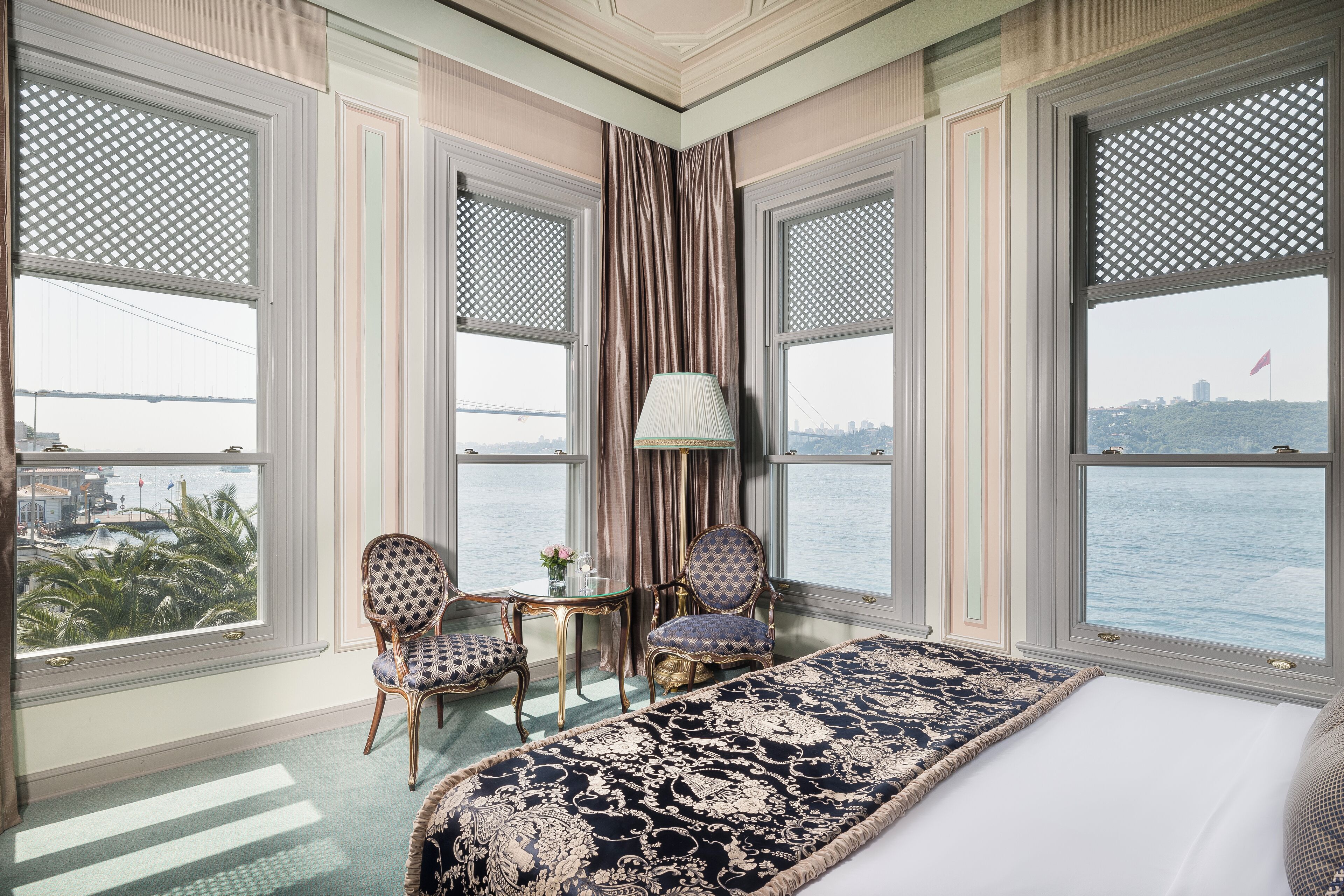A hotel room with a large bed, two chairs, a small table, and a view of a body of water and a bridge.