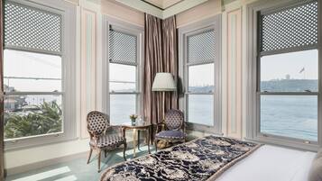 A hotel room with a large bed, two chairs, a small table, and a view of a body of water and a bridge.