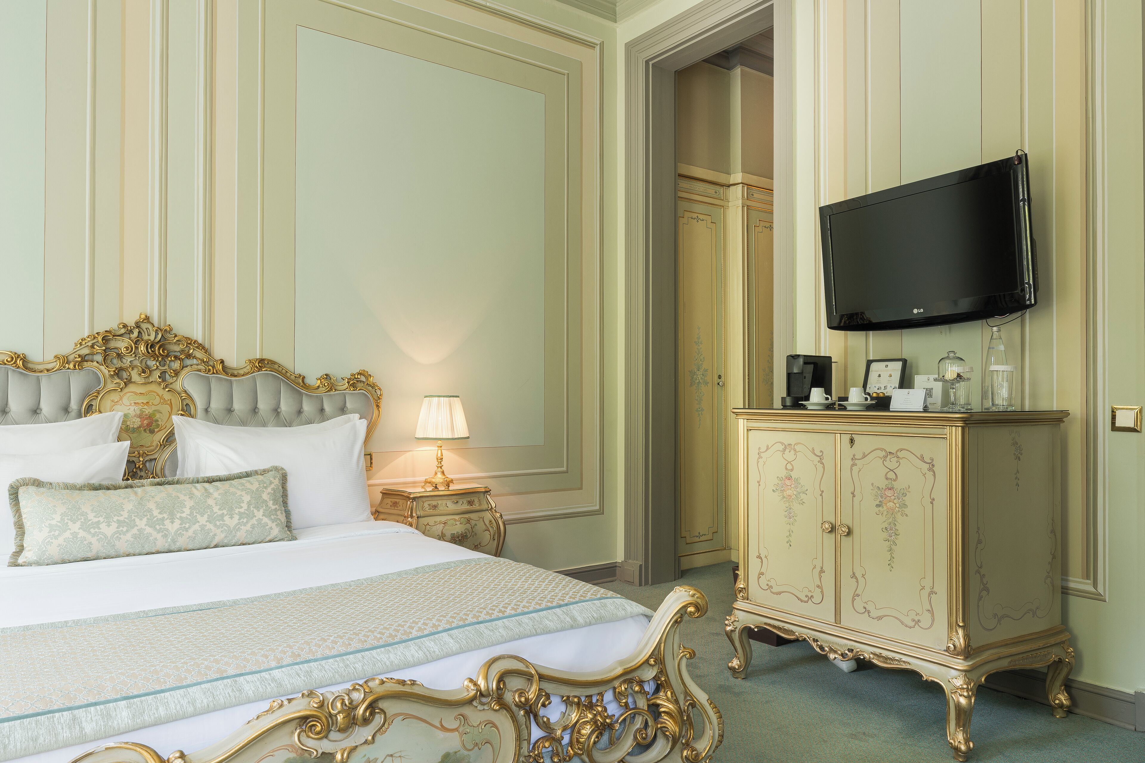 Una camera da letto lussuosa con un letto grande, decorazioni in oro elaborate, una televisione a parete e un classico armadio in legno.