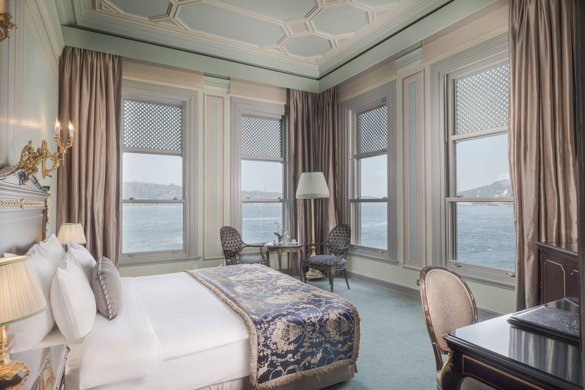 A hotel room with a large bed, two chairs, a small table, and a view of the sea.