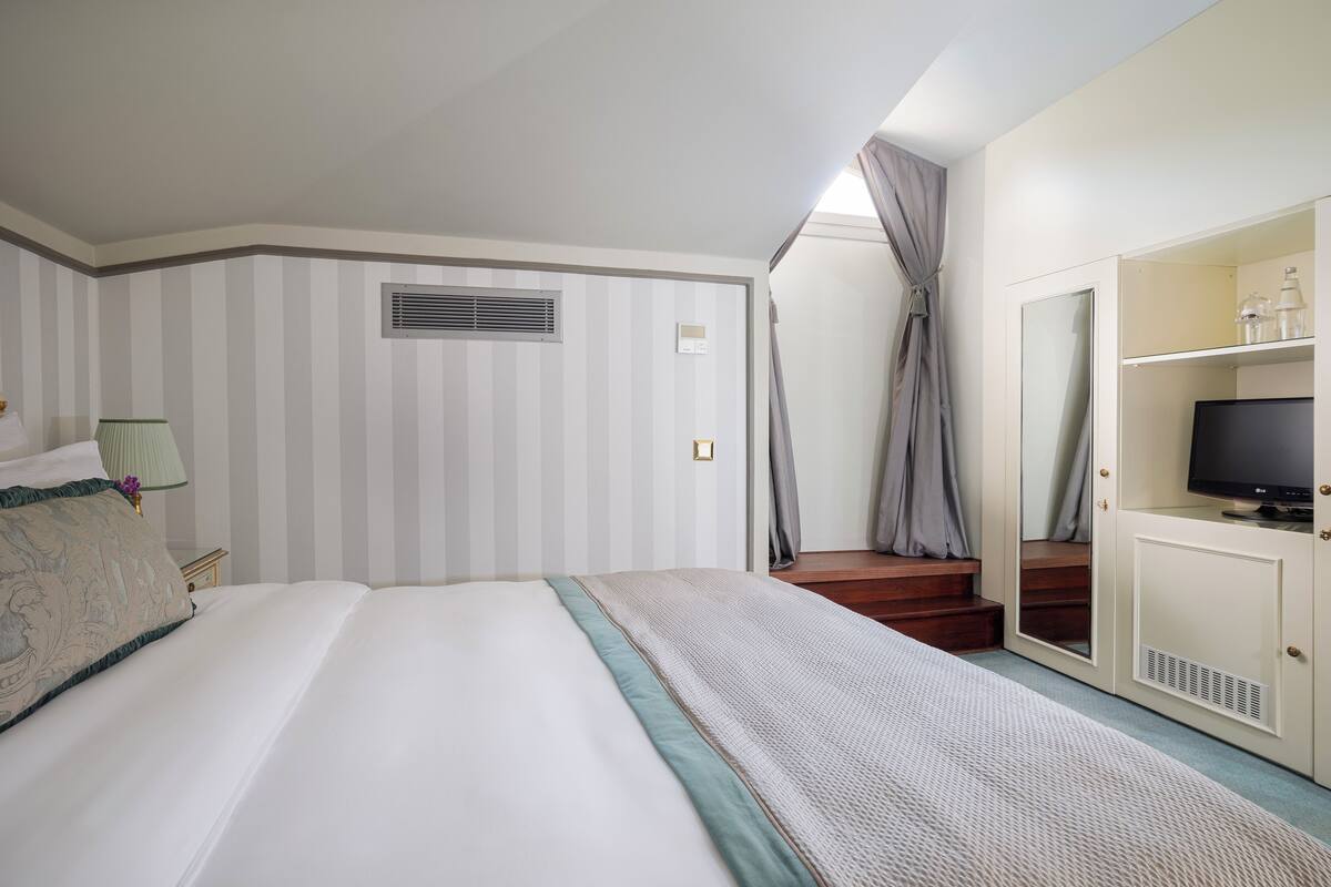 A hotel room with a bed, a TV, a wardrobe, and a window with curtains.