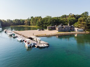 A lakeside dock with several boats moored, a stone pier, and a stone building with a chimney.