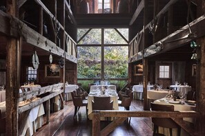 Cozy cabin-style dining area with a central table and individual settings, surrounded by high ceilings and large windows offering views of the surrounding greenery.