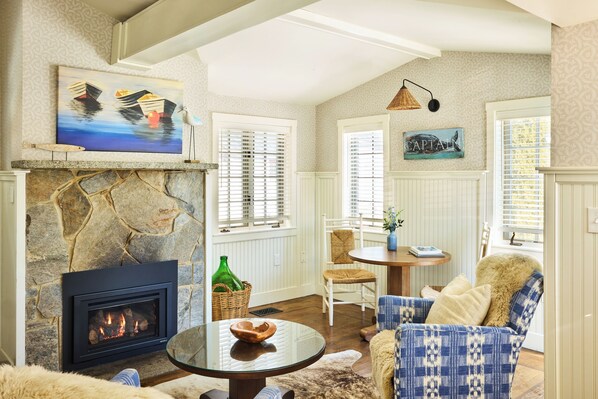 A cozy living room with a stone fireplace, wicker furniture, and a painting of boats on the wall.