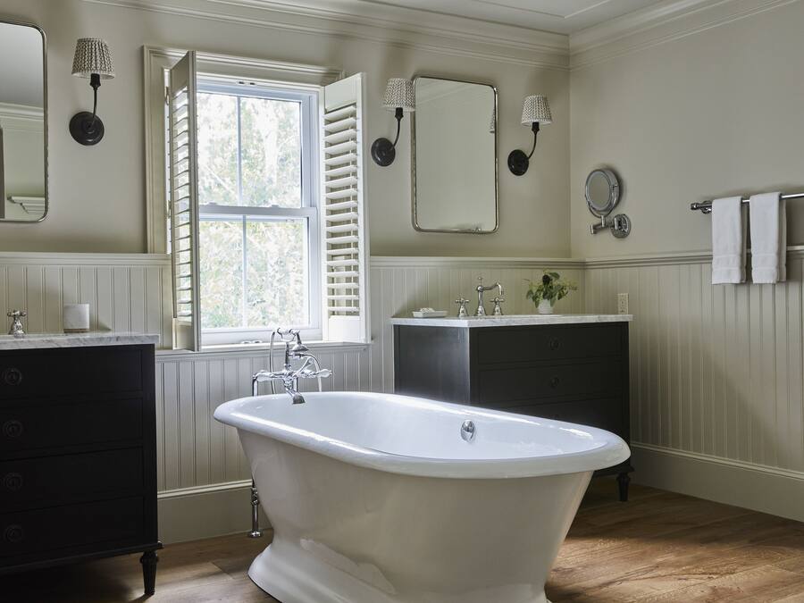 Un baño con una bañera independiente, un tocador con espejo y un ventanal con contraventanas.