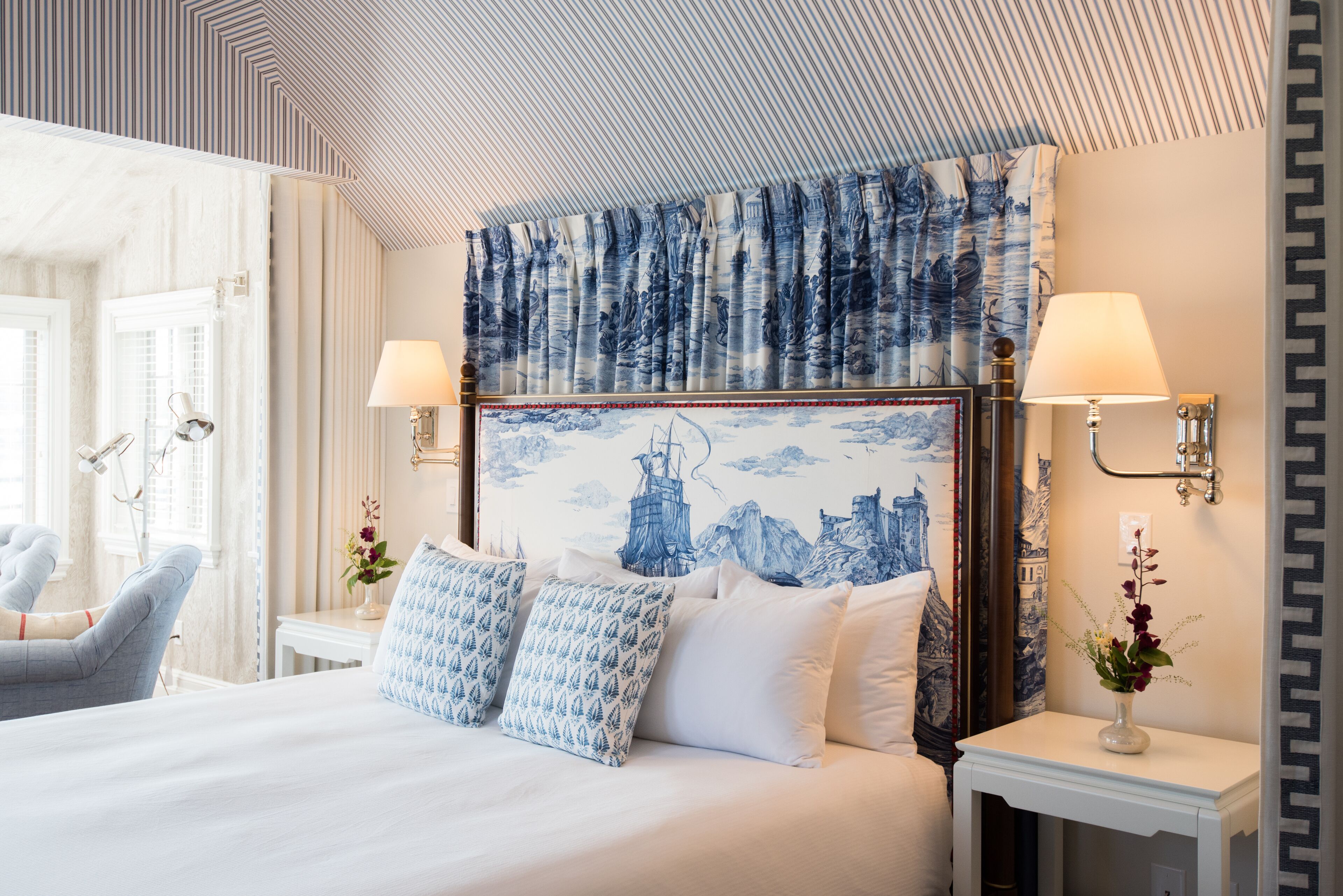Ett hotellrum med en stor säng, två sängbord med lampor, en stol och en vägg med en blå- och vitmönstrad sänggavel.