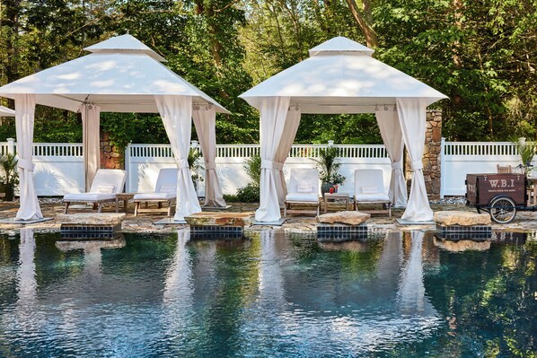 Relax by the serene pool surrounded by lush greenery and shaded gazebos.