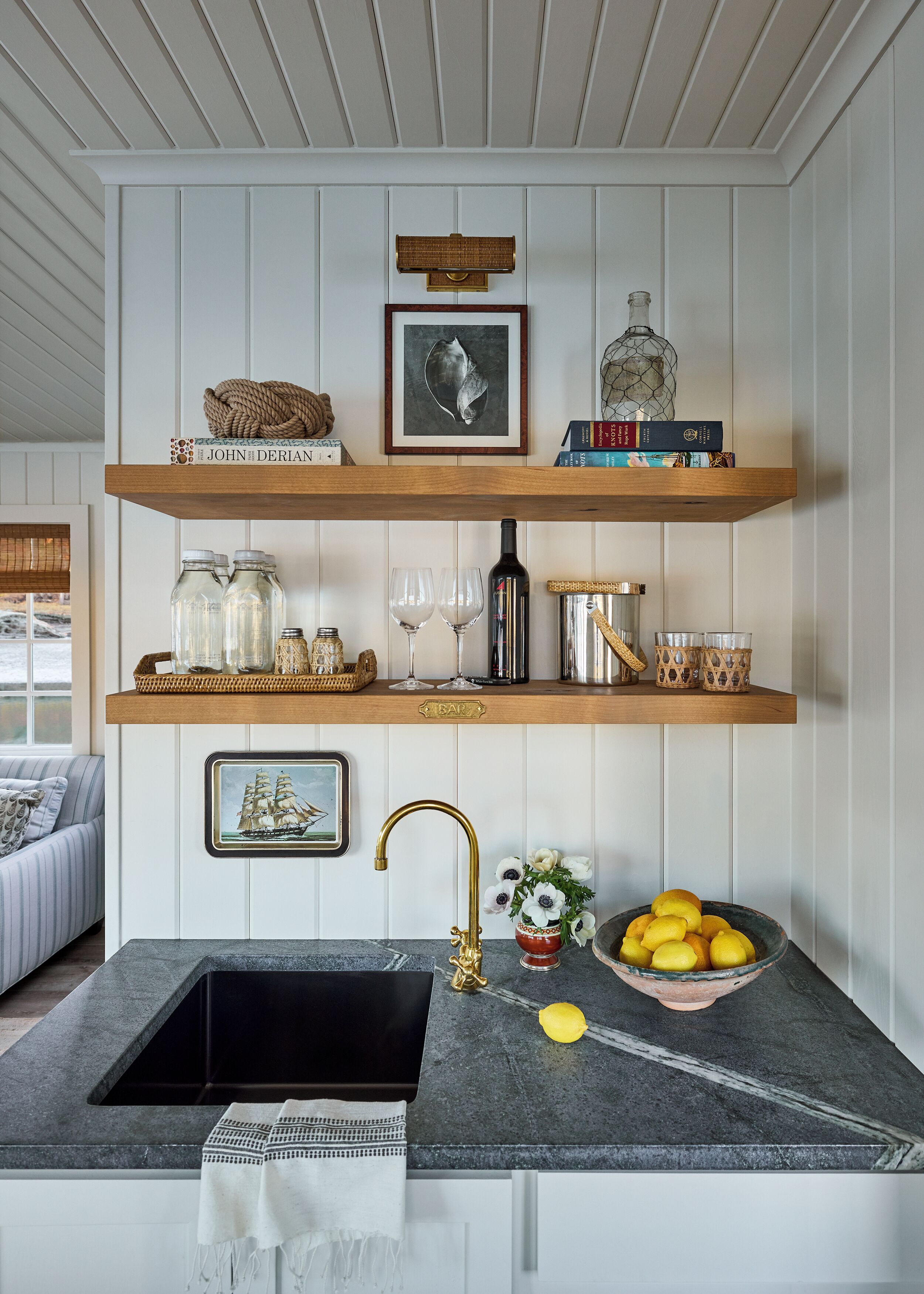 A kitchen with a black sink, wooden shelves, and a bar area.