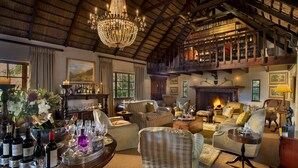 A spacious living room with a high ceiling, a chandelier, a fireplace, and a collection of bookshelves. - Hunter's Country House (Plettenberg Bay)