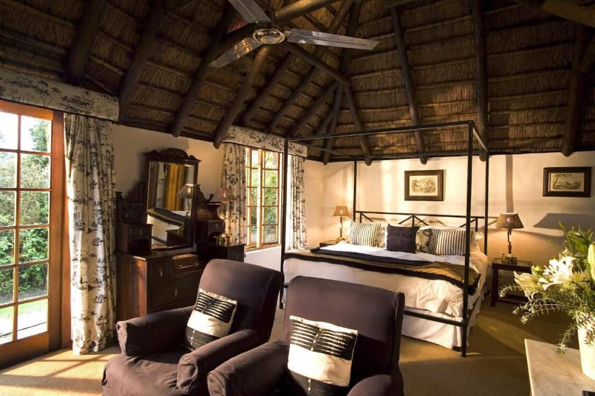 A room with a bed, two armchairs, a wooden dresser, and a large window with curtains.