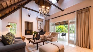 A spacious living room with a high ceiling, a chandelier, a fireplace, and a large sliding glass door leading to an outdoor area. - Hunter's Country House (Plettenberg Bay)