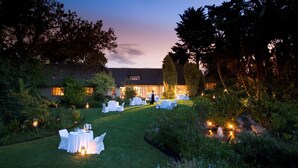 An outdoor garden setting with tables and chairs arranged for dining, surrounded by lush greenery and a building in the background. - Hunter's Country House (Plettenberg Bay)