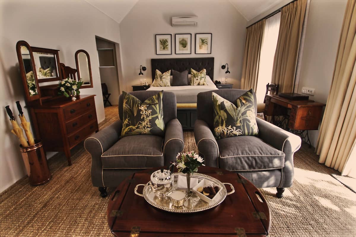 A hotel room with a bed, two armchairs, a coffee table with a tray, a dresser, and a mirror.