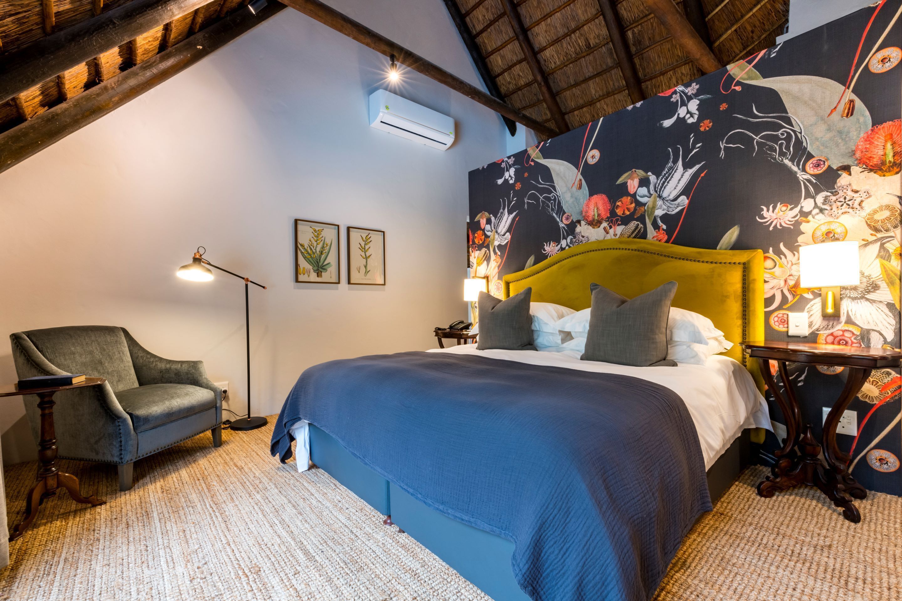 A bedroom with a bed, a chair, a lamp, and a wall with floral wallpaper.