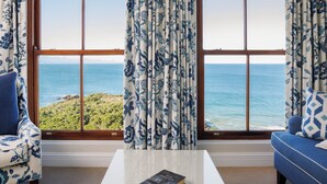 A room with a view of the ocean, a sofa, a chair, and a coffee table with a book. - The Plettenberg Hotel (Plettenberg Bay)