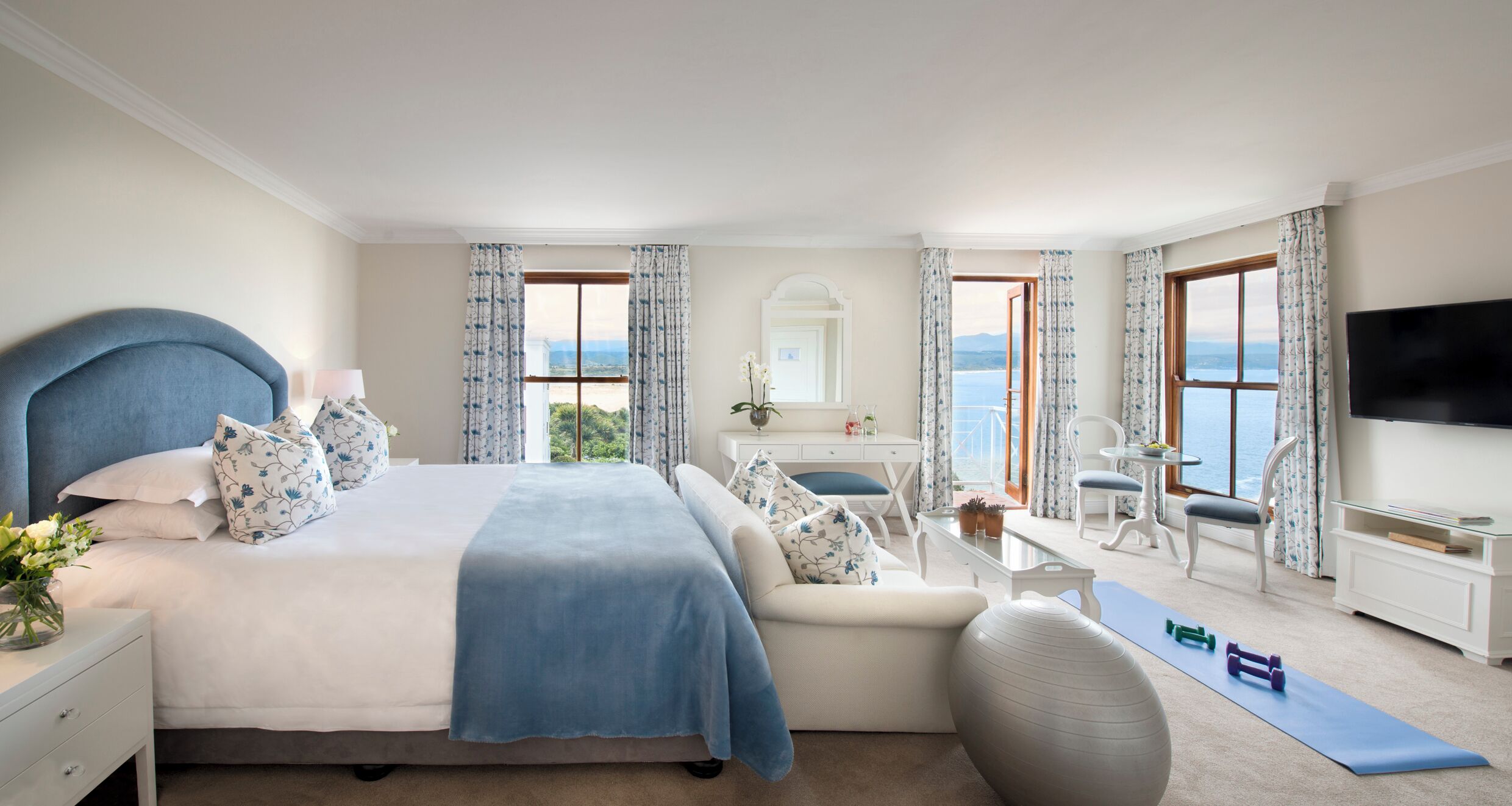 Une chambre à coucher avec un lit, un bureau, une chaise, une télévision et une vue sur la mer.