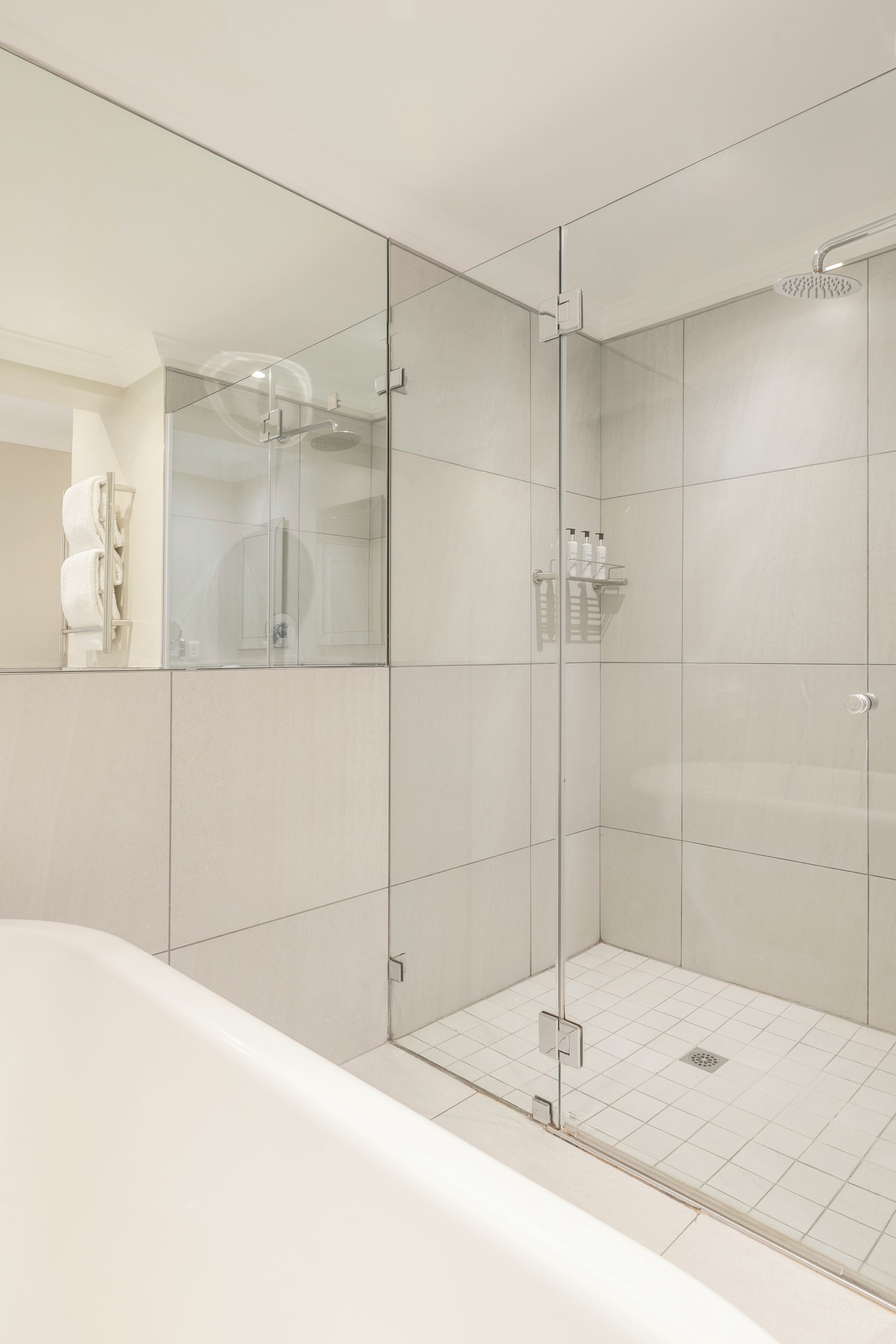 Een moderne badkamer met een douchecabine van glas, een wit bad en een handdoekrek.