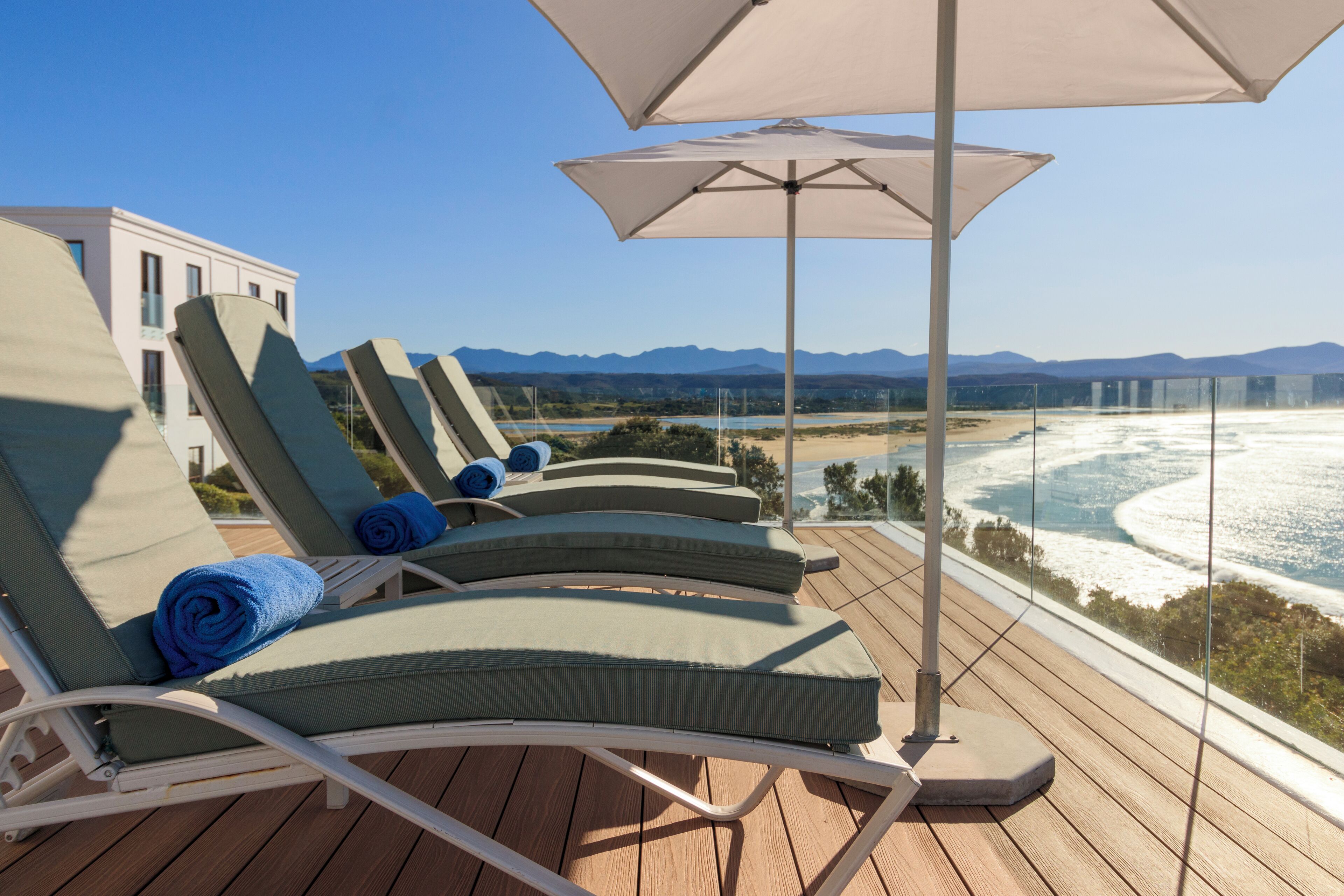 Une terrasse avec des chaises longues et des parasols, offrant une vue sur une plage et des montagnes.