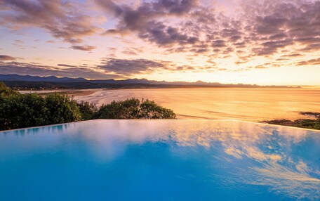 A pool with a view of a sunset over a body of water and distant mountains.
