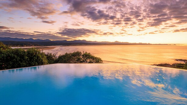 A pool with a view of a sunset over a body of water and distant mountains. - The Plettenberg Hotel (Plettenberg Bay)