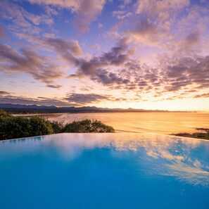 A pool with a view of a sunset over a body of water and distant mountains. - The Plettenberg Hotel (Plettenberg Bay)