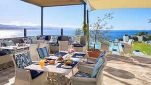 An outdoor seating area with wicker furniture, a table with a drink, and a view of the sea. - The Plettenberg Hotel (Plettenberg Bay)