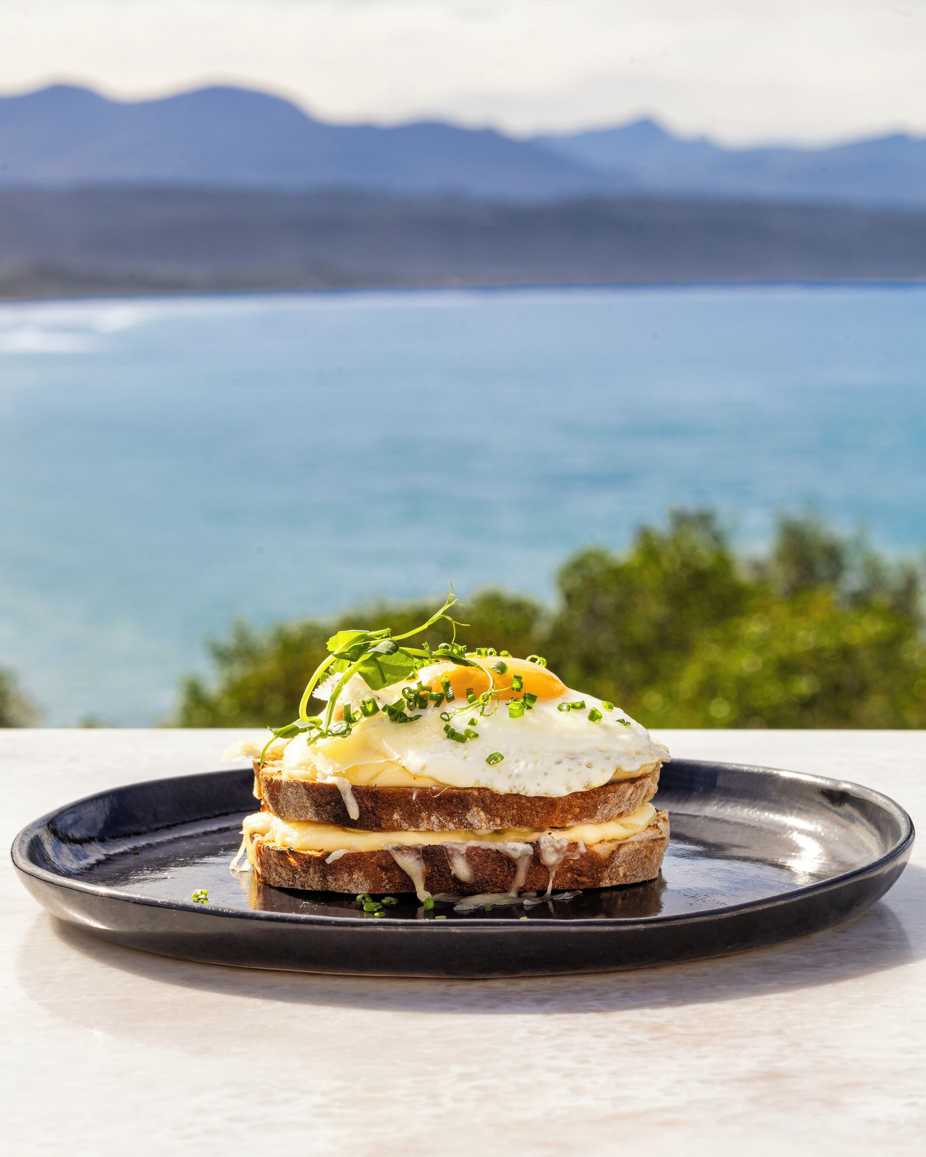 A sandwich on a plate with a scenic view of mountains and water in the background.
