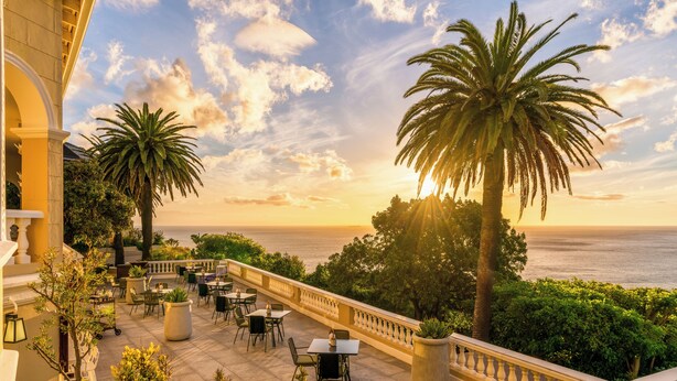 A terrace with outdoor seating, palm trees, and a view of the sea. - Ellerman House (Cape Town)
