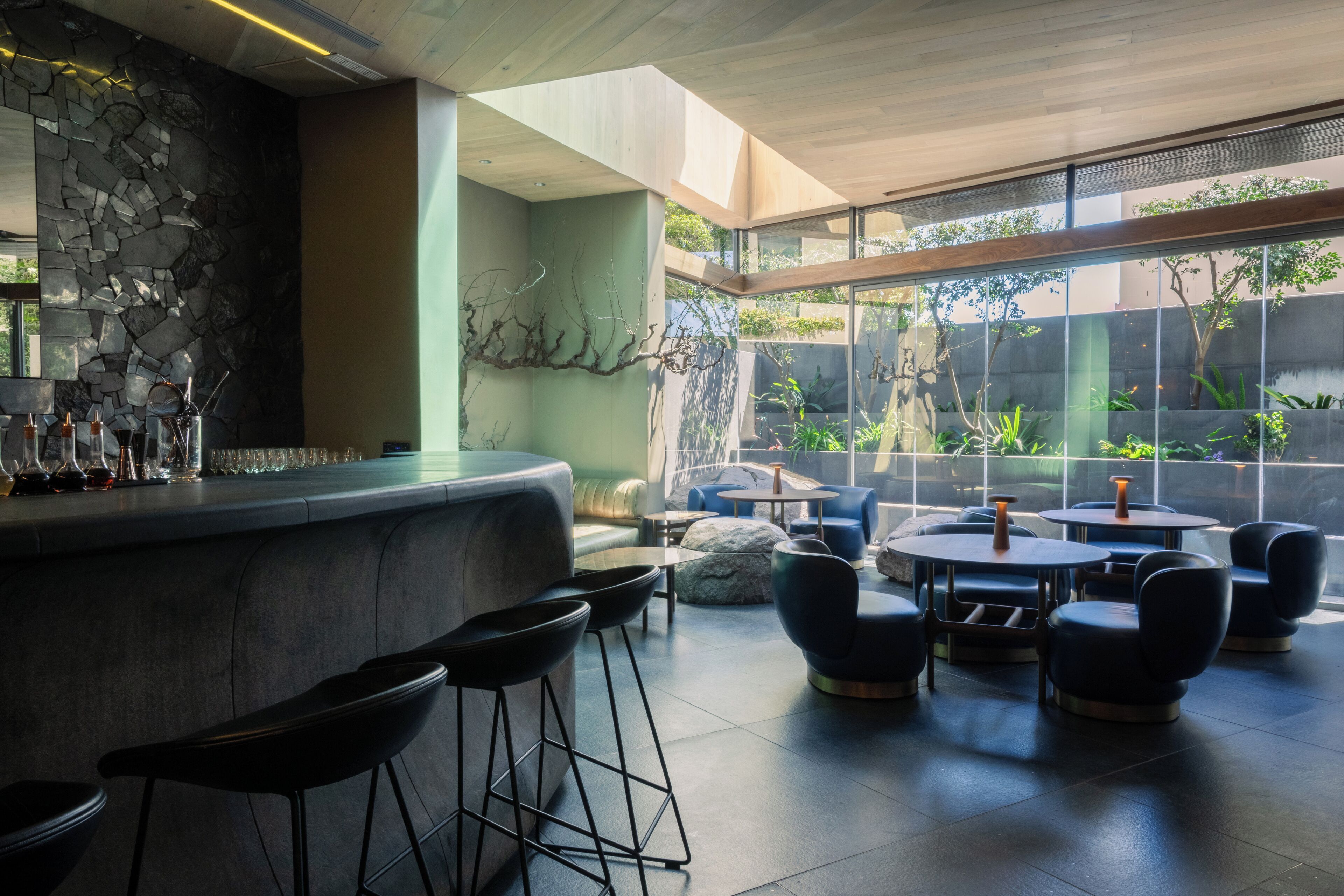 A modern bar area with a stone wall, bar stools, and round tables with chairs.