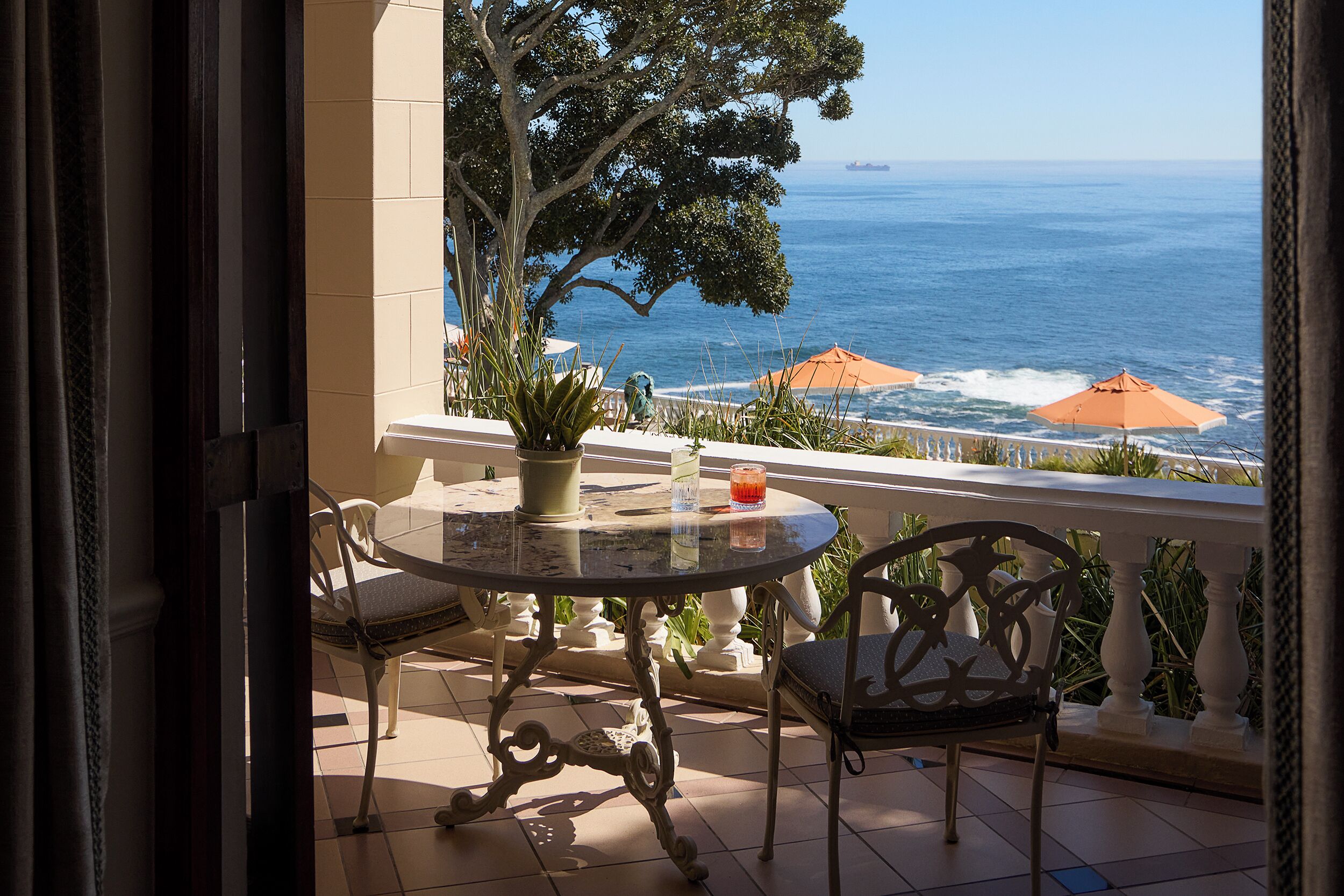 A balcony with a table and chairs, overlooking the sea.