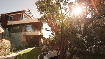 A modern two-story house with a stone facade, a curved pathway, and a small pond.
