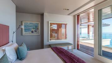 Un dormitorio moderno con una cama grande, dos cuadros, un banco y un balcón con vistas al mar.