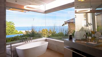 A modern bathroom with a freestanding bathtub, a large mirror, and a view of the sea.