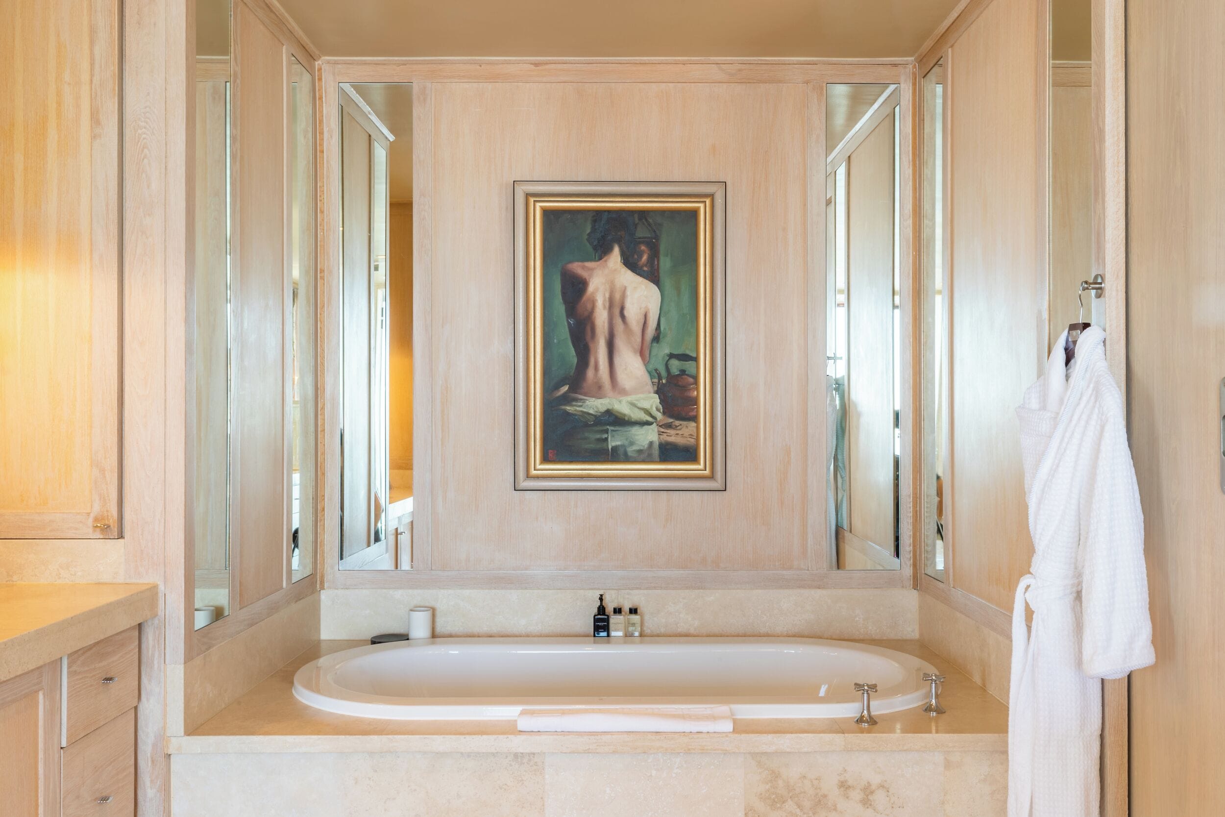 A bathroom with a large bathtub, a framed painting on the wall, and a towel hanging on the wall.