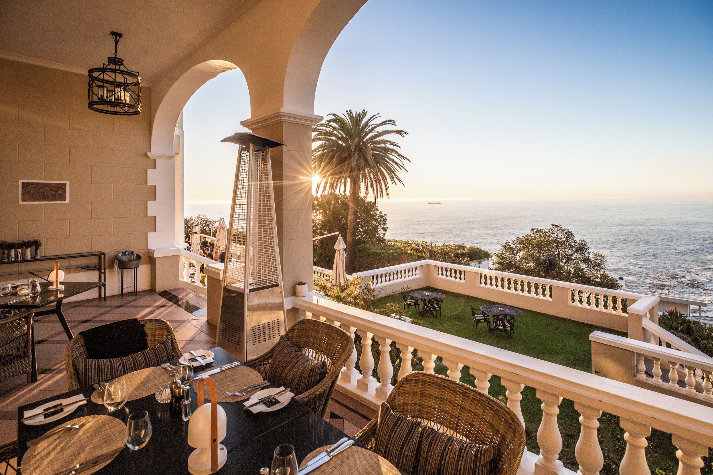 A terrace with wicker furniture, a dining table set, and a view of the sea.