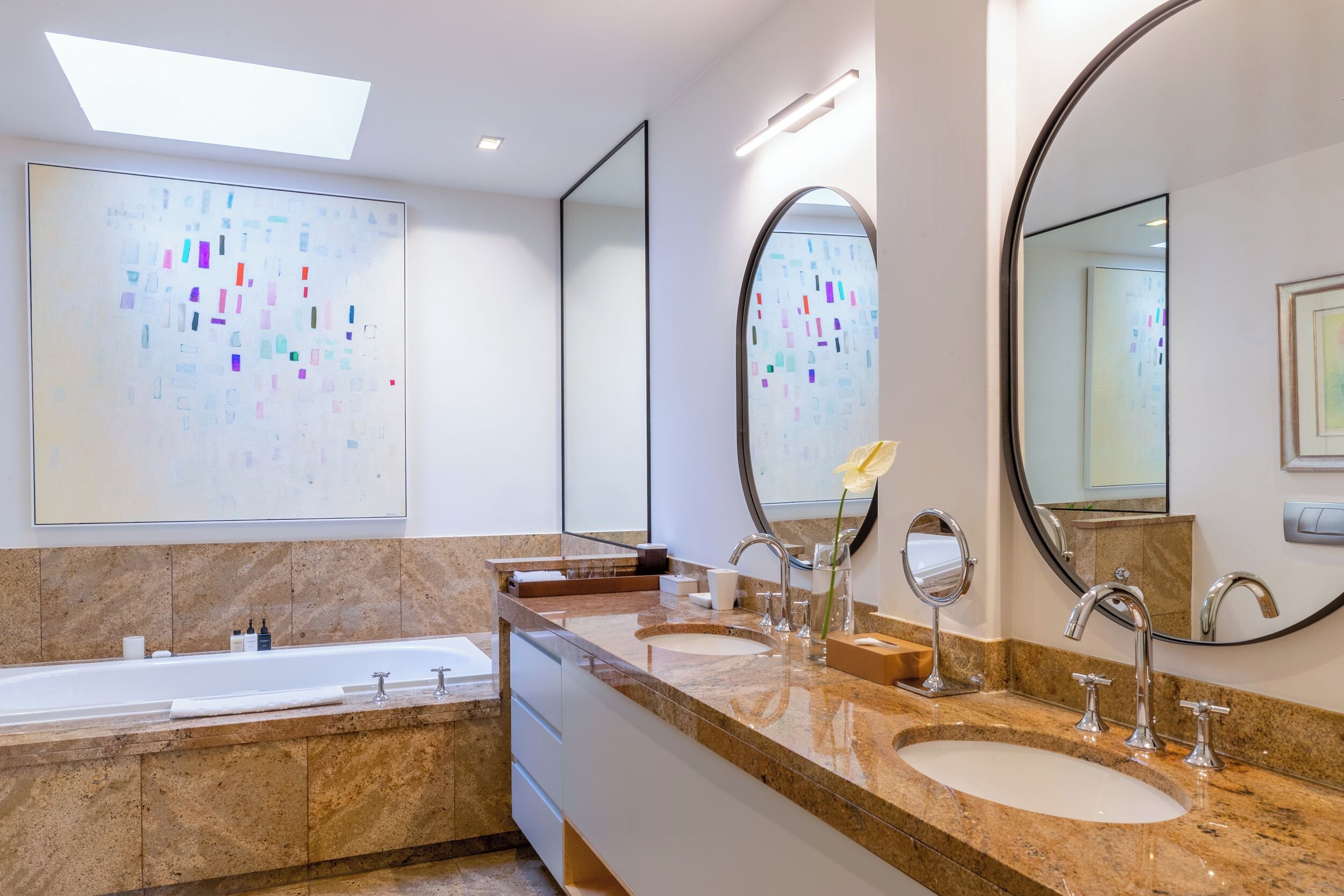 A modern bathroom with a large skylight, two sinks, a bathtub, and multiple mirrors.